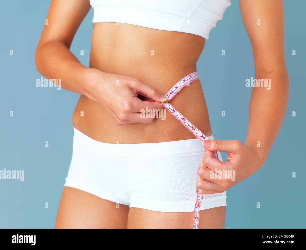 Cropped view of young woman measuring her waist with tape measure