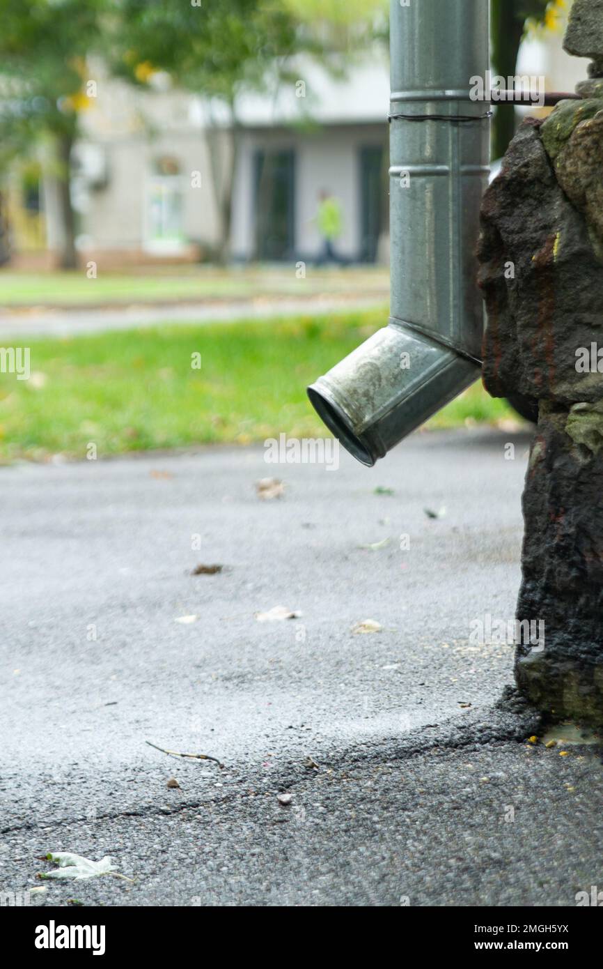 Drain pipes and asphalt sidewalk. Bottom of downspout.  Vertical orientation. Stock Photo