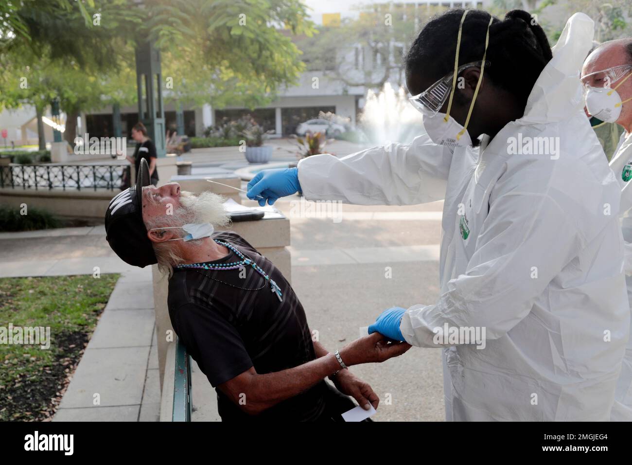 Nurse practitioner Gregory Pierre, right, holds the hand of Leonardo Toledo  Martinez, who is homeless, as he is tested for COVID-19 in a program  administered by the Miami-Dade County Homeless Trust during