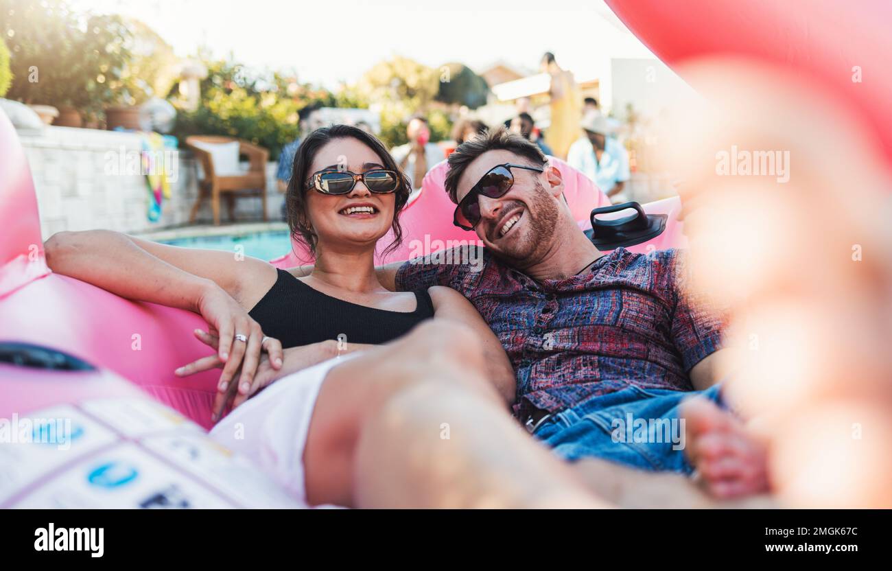 Couple, relax and smile for pool party on inflatable floating in the water enjoying summer vacation together. Happy man and woman relaxing in swimming Stock Photo