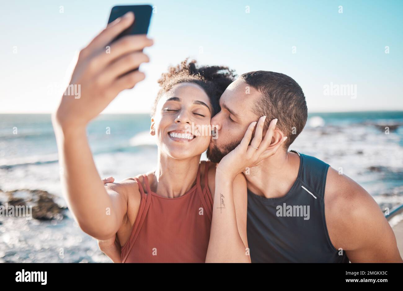 Selfie kiss, gratitude and couple with a phone for streaming, training and love at the beach in Bali. Caring, exercise and affectionate man and woman Stock Photo