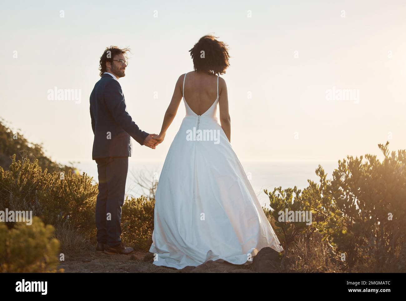 Love, wedding and holding hands with couple in nature park for celebration, romance and happiness. Sunset, support and summer with bride and groom in Stock Photo