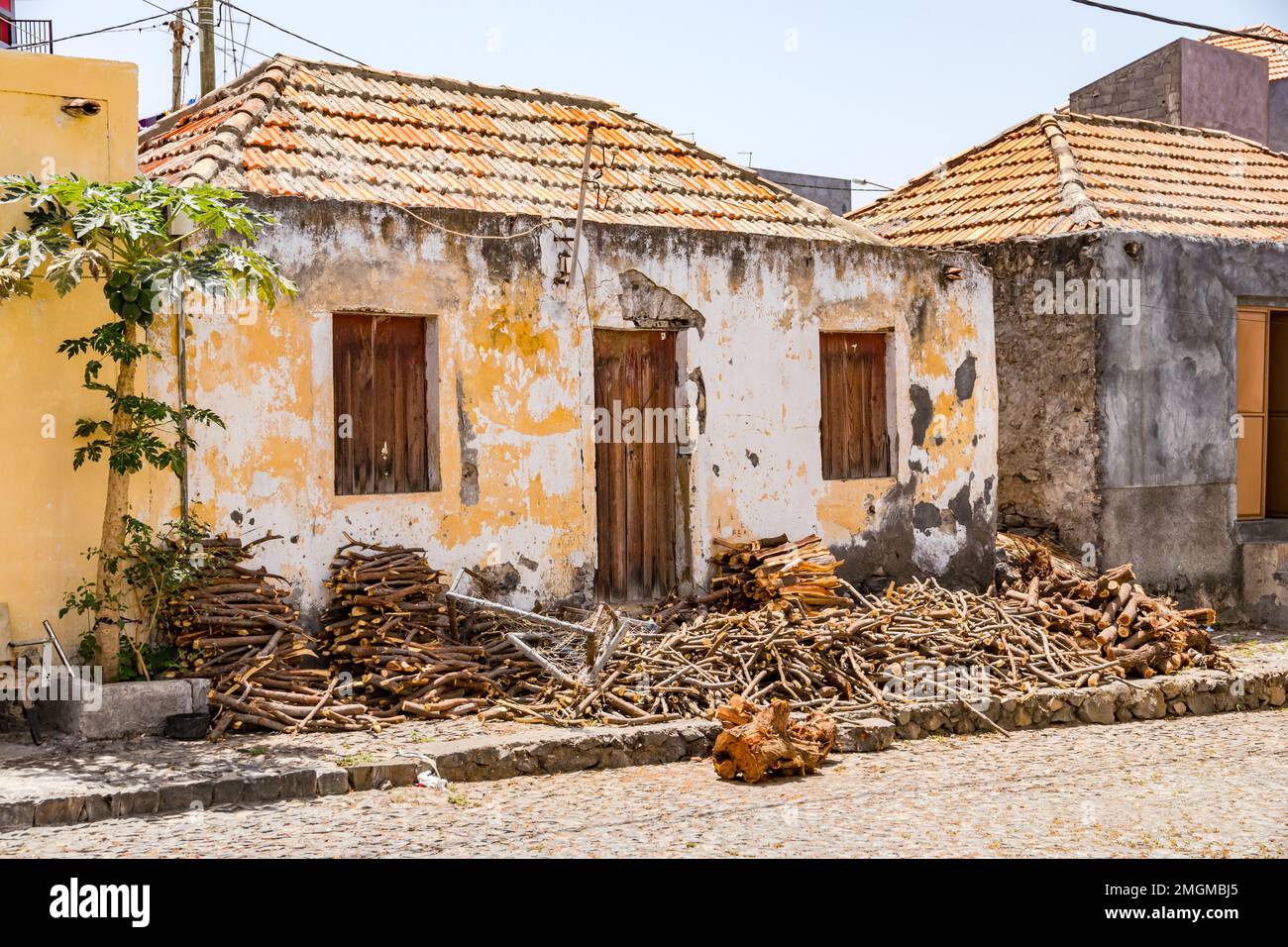 A dilapidated stone cottage with logs and firewood in front of the front door and on the sidewalk, Fogo Island, Cape Verde Stock Photo