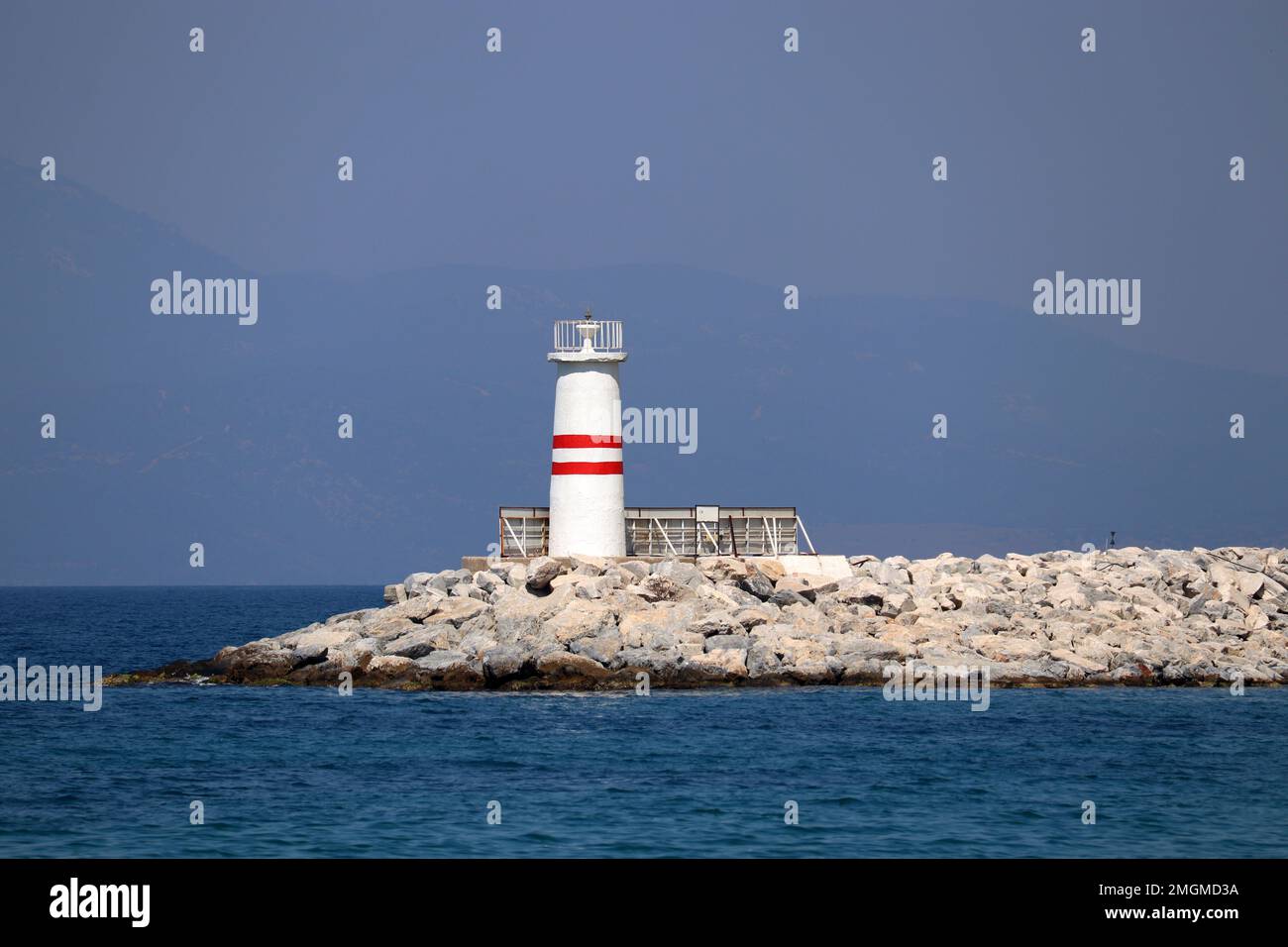 Lighthouse tower on a stone pier in azure sea against misty mountains Stock Photo