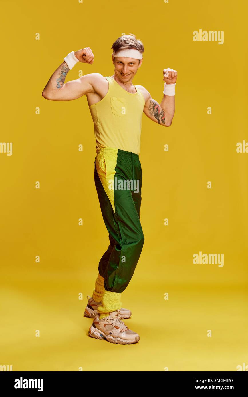 Portrait of young cheerful man in sports uniform posing, showing muscles over bright yellow studio background. Concept of emotions, lifestyle, sport Stock Photo