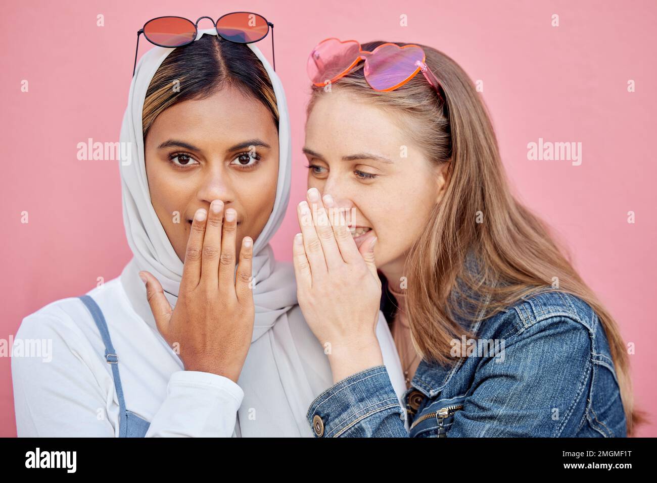 Woman, friends and secret whisper of gossip in shock against a pink studio background. Women sharing secrets, rumor or surprise whispering in the ears Stock Photo