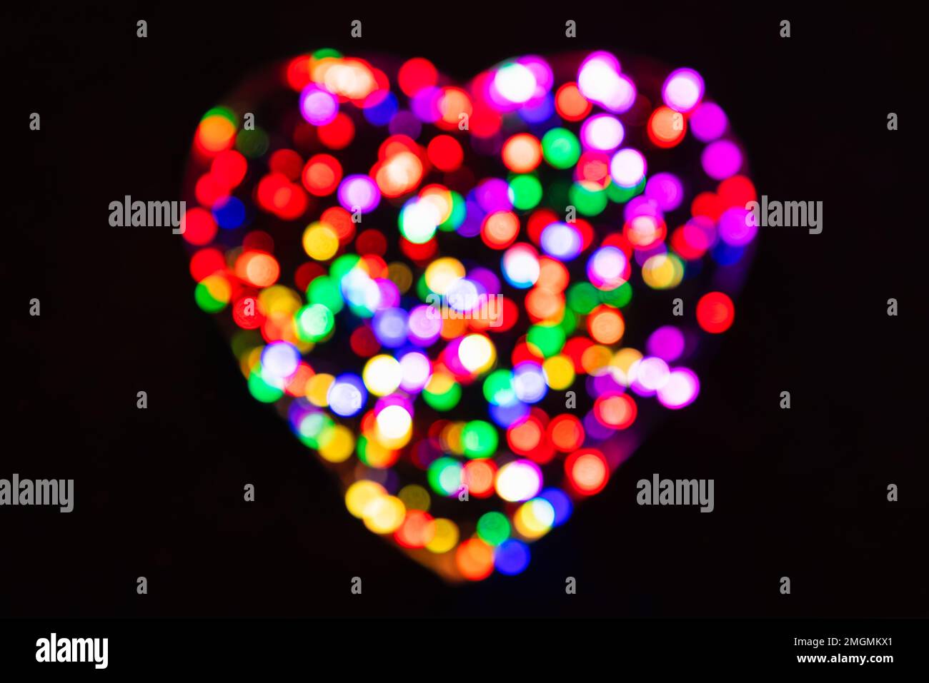 Rainbow defocused confetti circles from the light in the shape of a heart on a black background with bokeh effect Stock Photo