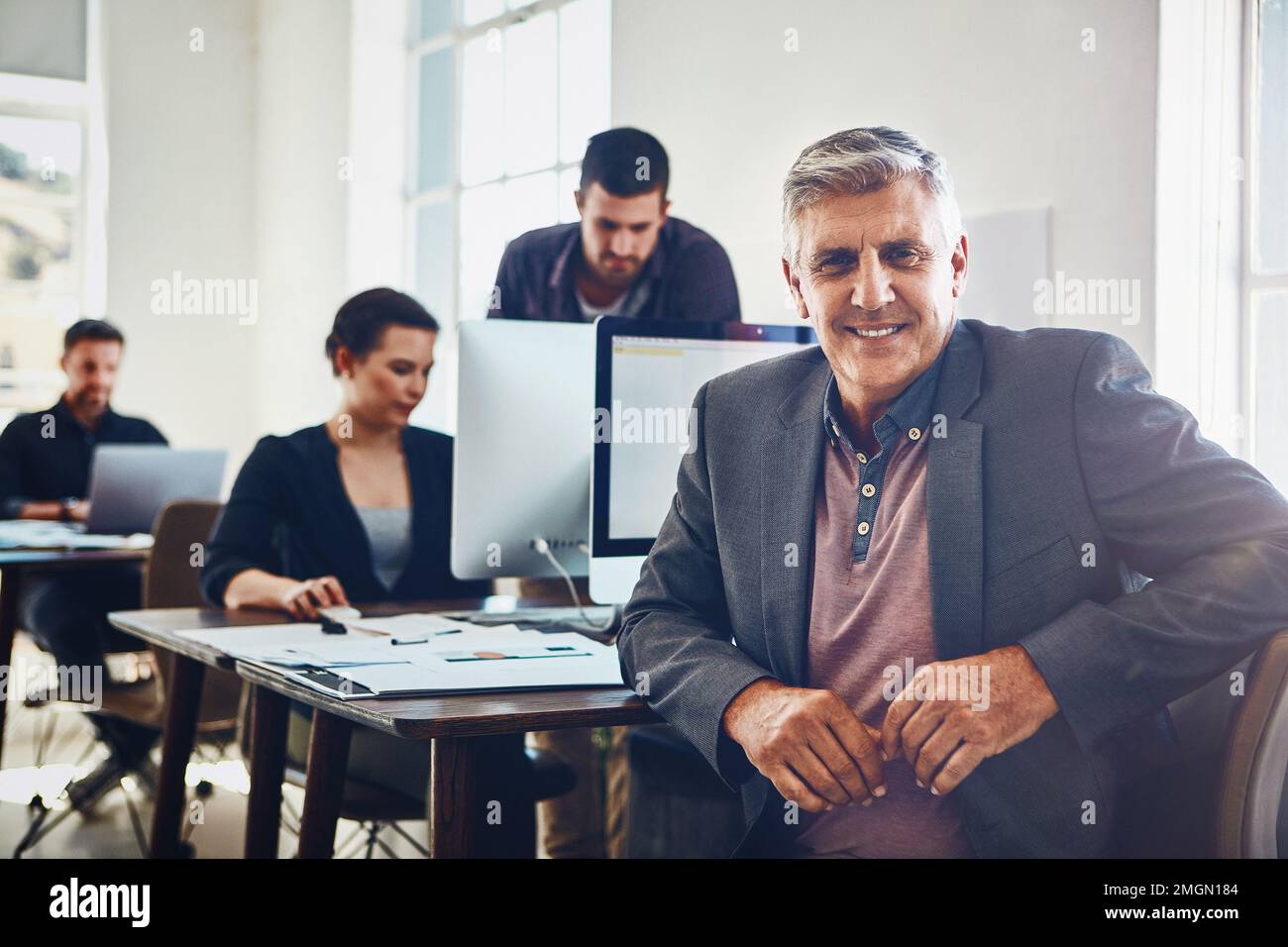 Senior, portrait and business man in office or company workplace. Leadership, ceo and happy elderly male employee or manager with colleagues working Stock Photo