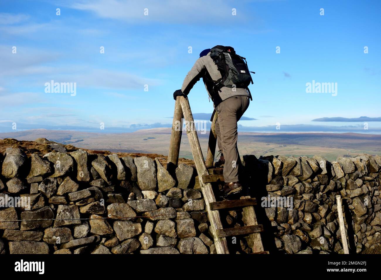 Man Climbing Wooden Ladder Stile over Stone Wall on the Summit of