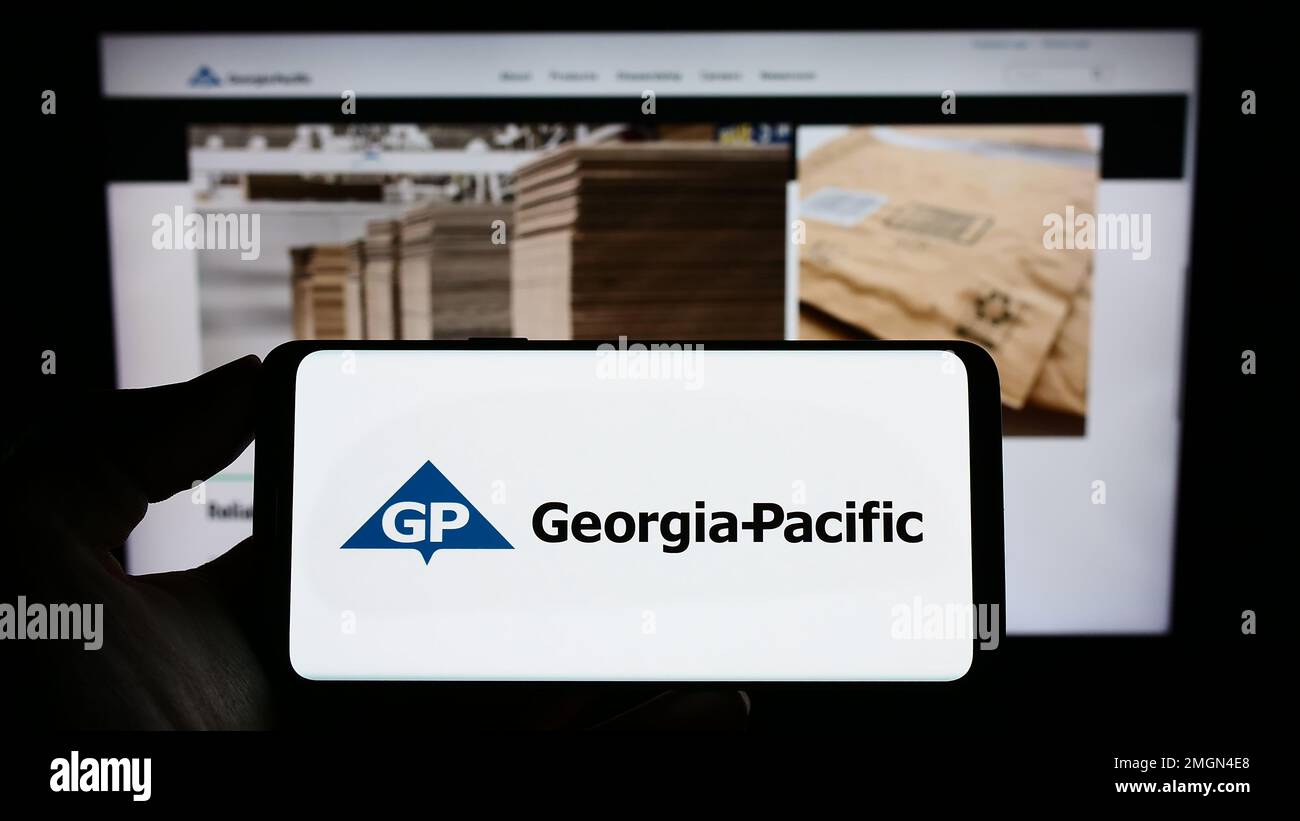Person holding cellphone with webpage of US pulp and paper company Georgia-Pacific on screen in front of business logo. Focus on phone display. Stock Photo