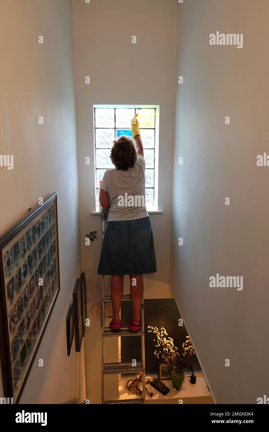 A woman on a step ladder cleaning the windows inside the house Stock Photo Alamy