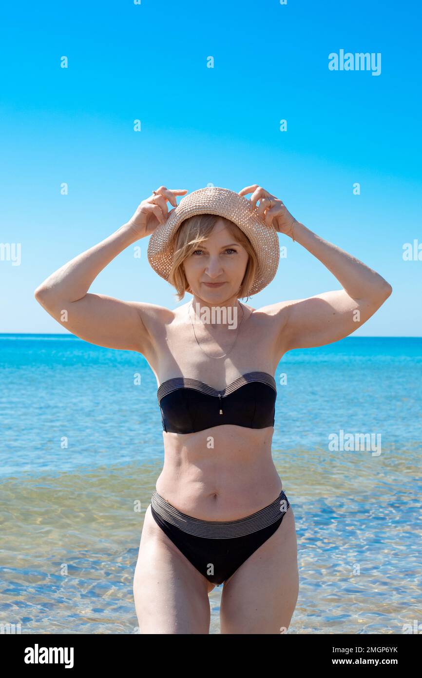 A mature, slender woman in a swimsuit at sea on a sunny day, holding a hat  with her hands. Summer vacation at the seaside Stock Photo - Alamy