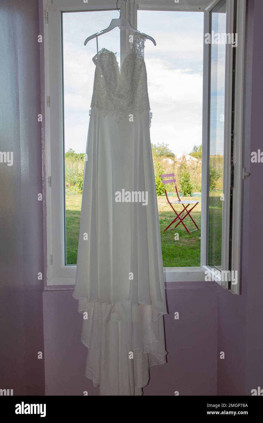 wedding dress hanging on a hanger at the window Stock Photo