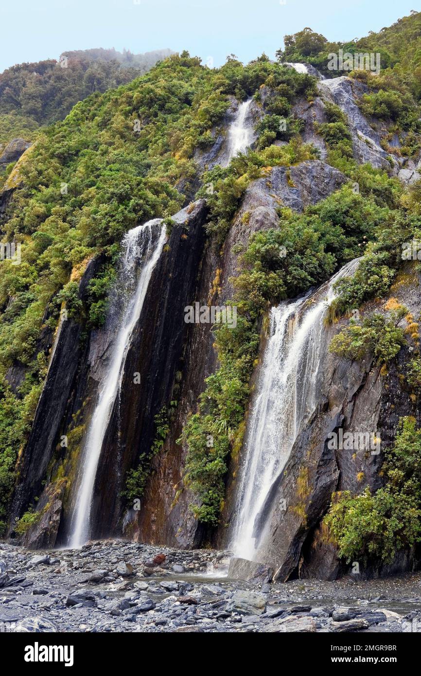 waterfalls; hillside; rock; green vegetation; nature, Franz Josef Glacier; Westland Tai Poutini National Park; Franz Josef; New Zealand; vertical Stock Photo