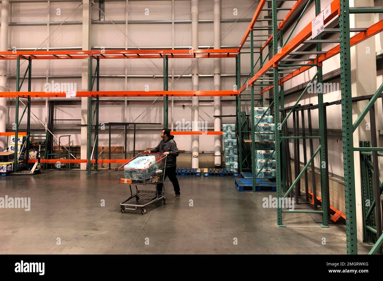 A customer walks past mostly empty shelves that normally hold toilet