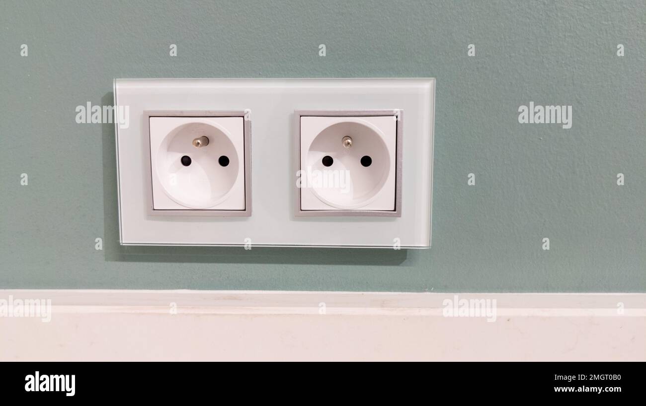 two white french european electrical outlets with plug inserted into