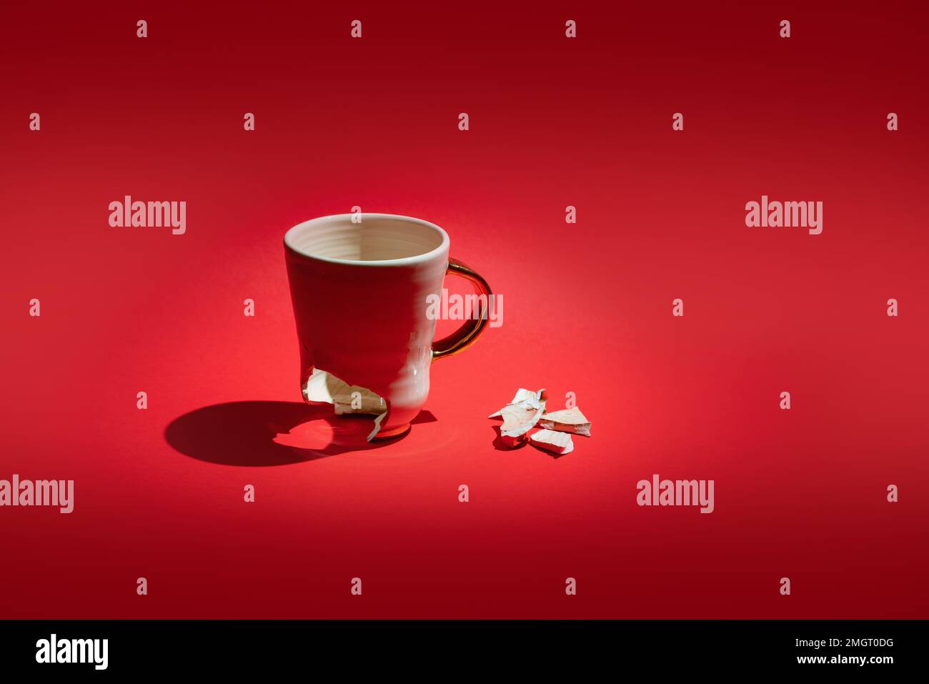 Broken tea cup isolated on red background. Cracked coffee mug and fragile ceramic pieces Stock Photo
