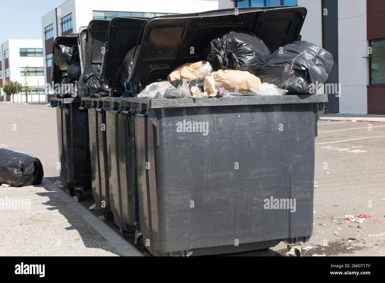 three big gray bins in the street full and overflowing with garbage bag