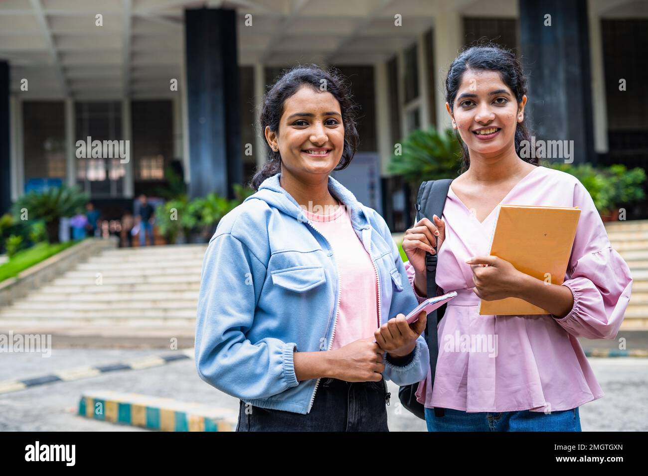 Happy smiling students standing by holding books while looking camera at college campus - concept of knowledge, friendship and learning. Stock Photo