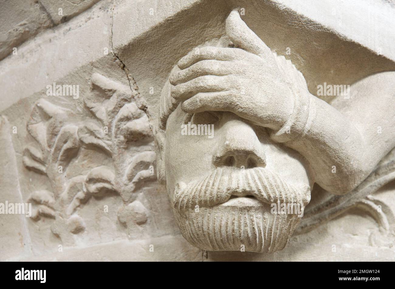 Carved stone grotesque head of a man apparently suffering from a headache, on a 12th century pillar in St John the Baptist Church, Bere Regis, Dorset. Stock Photo