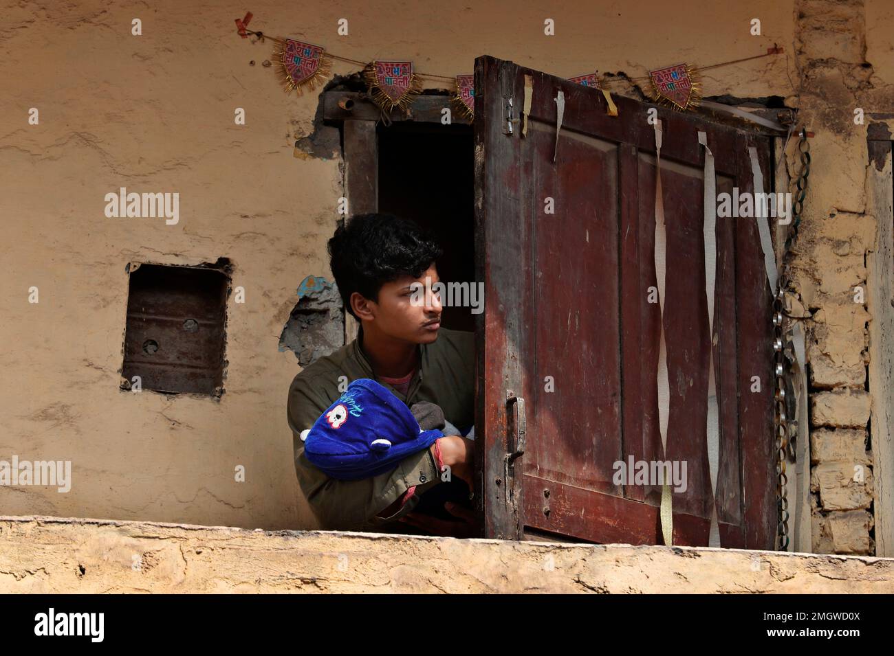 A man carrying a new born baby looks out from the balcony of his house ...