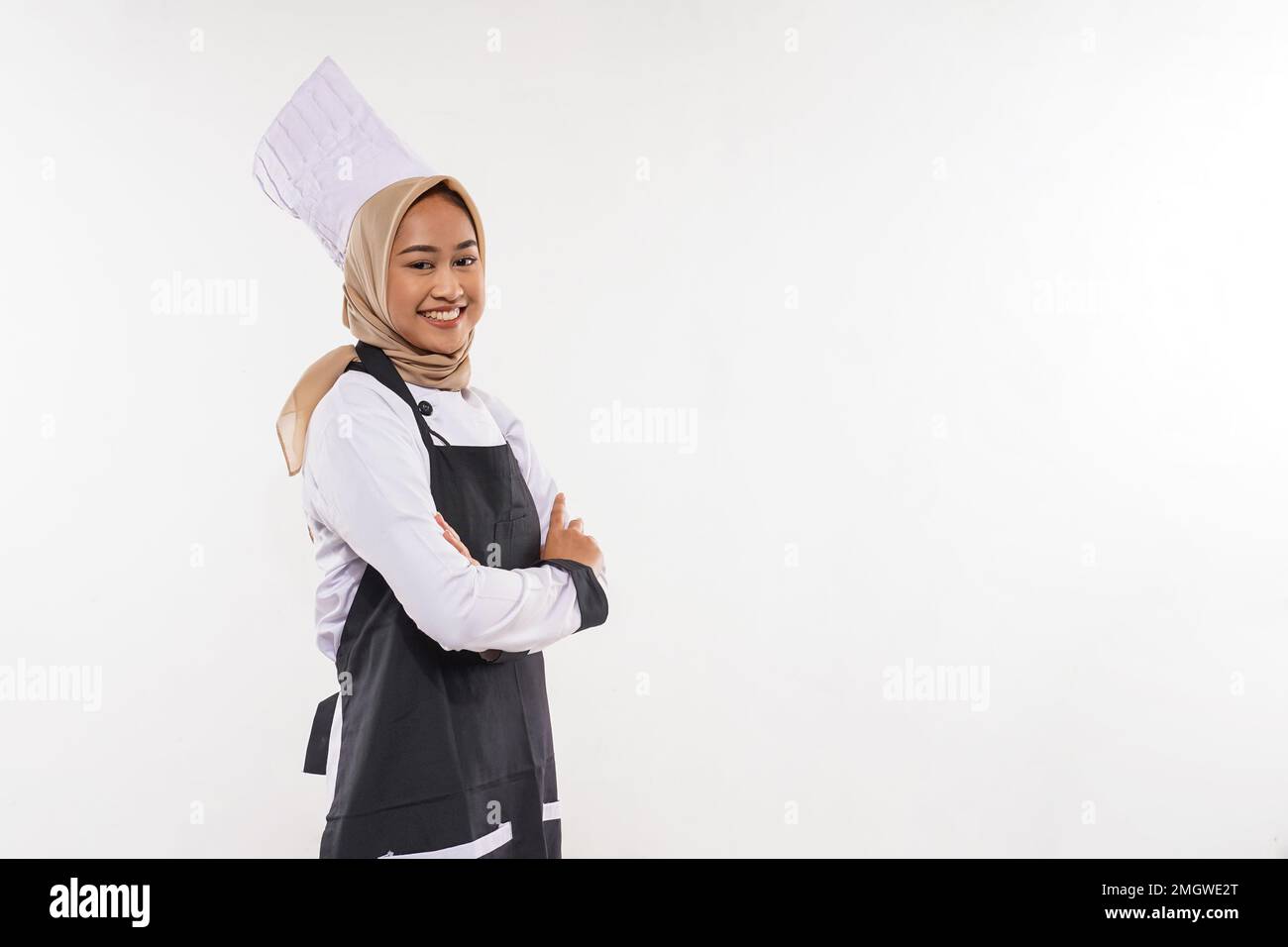 a young cook in apron with hijab standing with hands crossed Stock