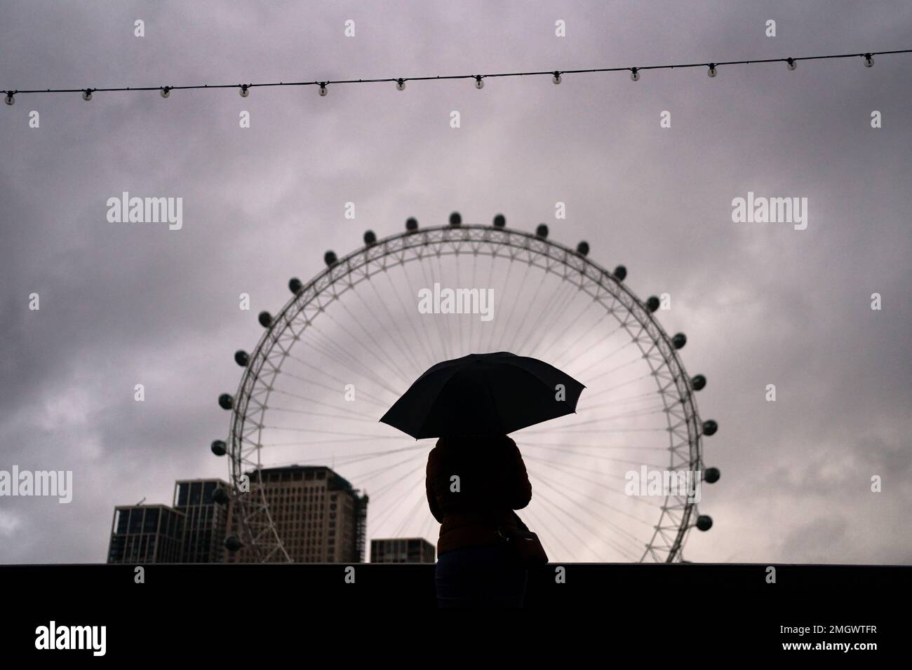 A woman covers up against the wet and windy weather on the Embankment opposite the London Eye in central London. Picture date: Thursday January 26, 2023. Stock Photo