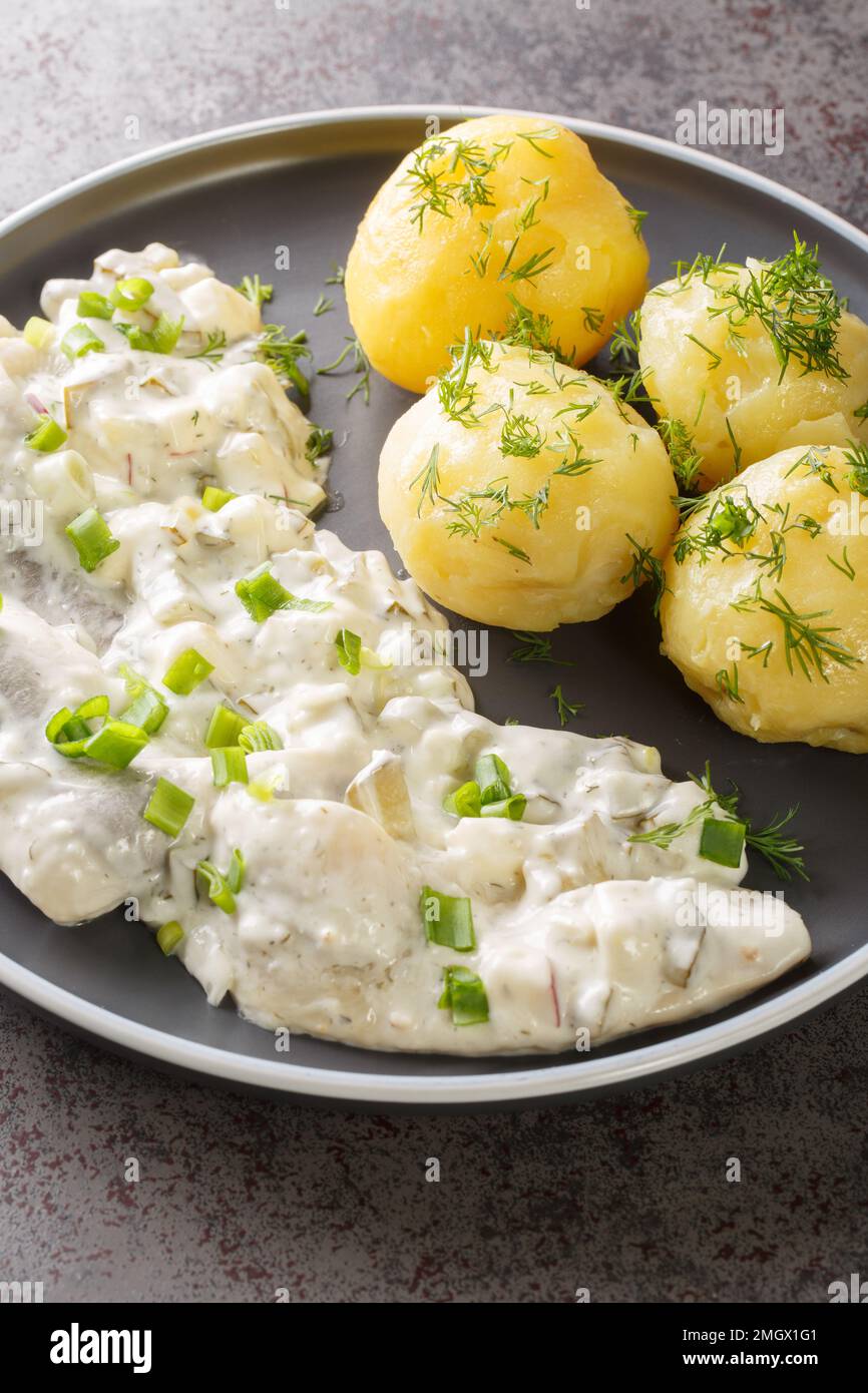 Sahnehering is a German dish with pickled Herrings fillets, apples and onion in a spiced marinade of cream served with boiled potato closeup on the pl Stock Photo