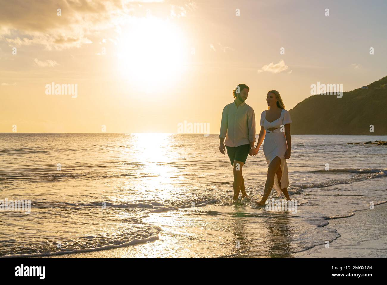 Happy couple walking along waterfront sandy beach on a tropical island ...
