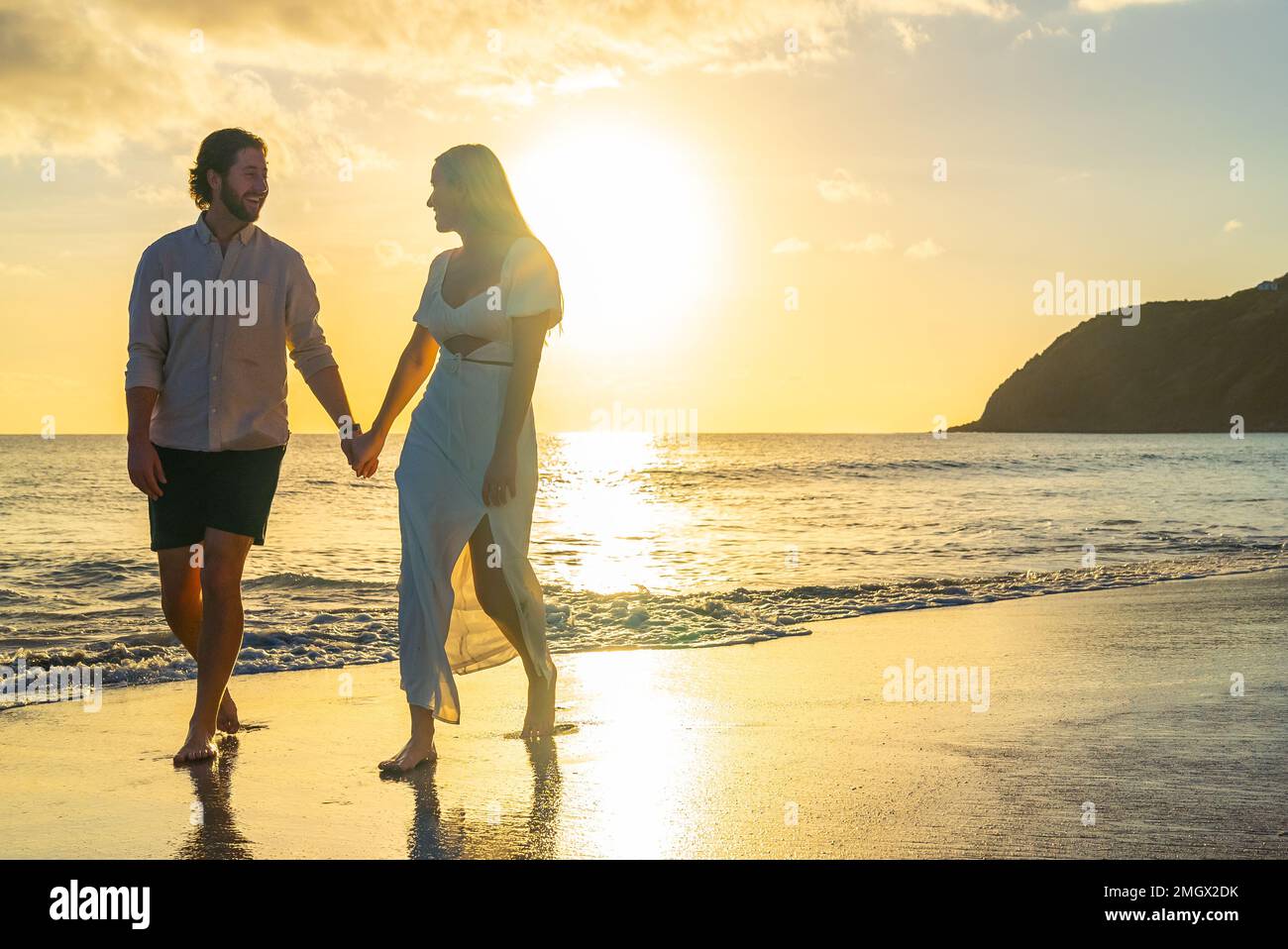 Happy couple walking along waterfront sandy beach on a tropical island ...