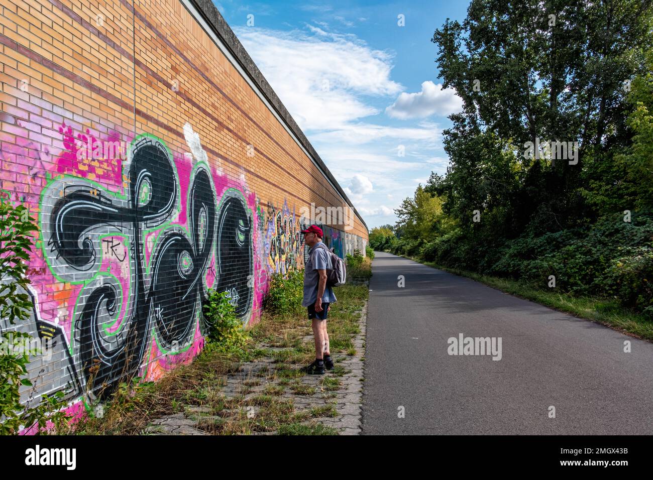 Senior man on Hiking & Biking path on Route of former Berlin Wall ,Baumschulenweg,Treptow-Köpenick,Berlin. Graffiti covered wall Stock Photo