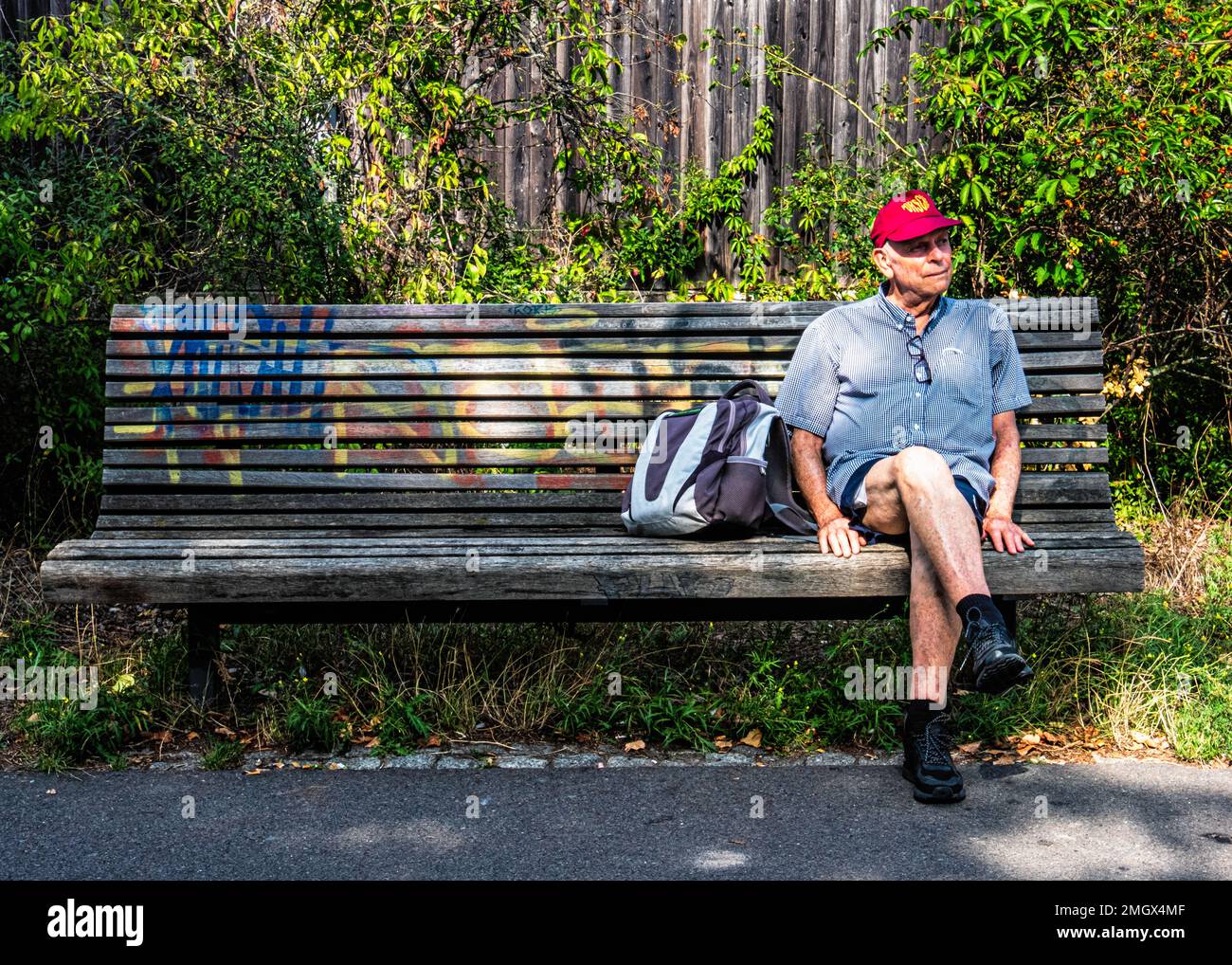Senior man rests on bench next to Hiking & Biking path on Route of former Berlin Wall ,Baumschulenweg,Treptow-Köpenick,Berlin. Stock Photo