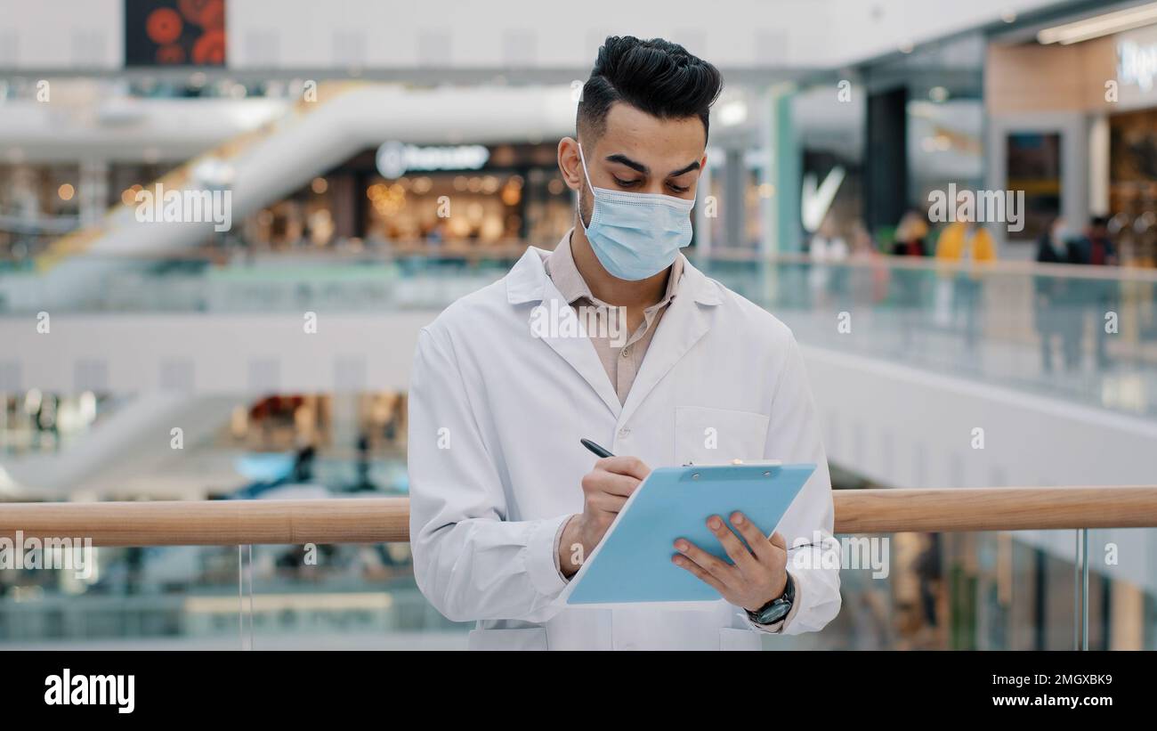 Ethnic Indian inspector scientist doctor medical male worker man writing in papers documents expertise check health safety rules supervisor with Stock Photo