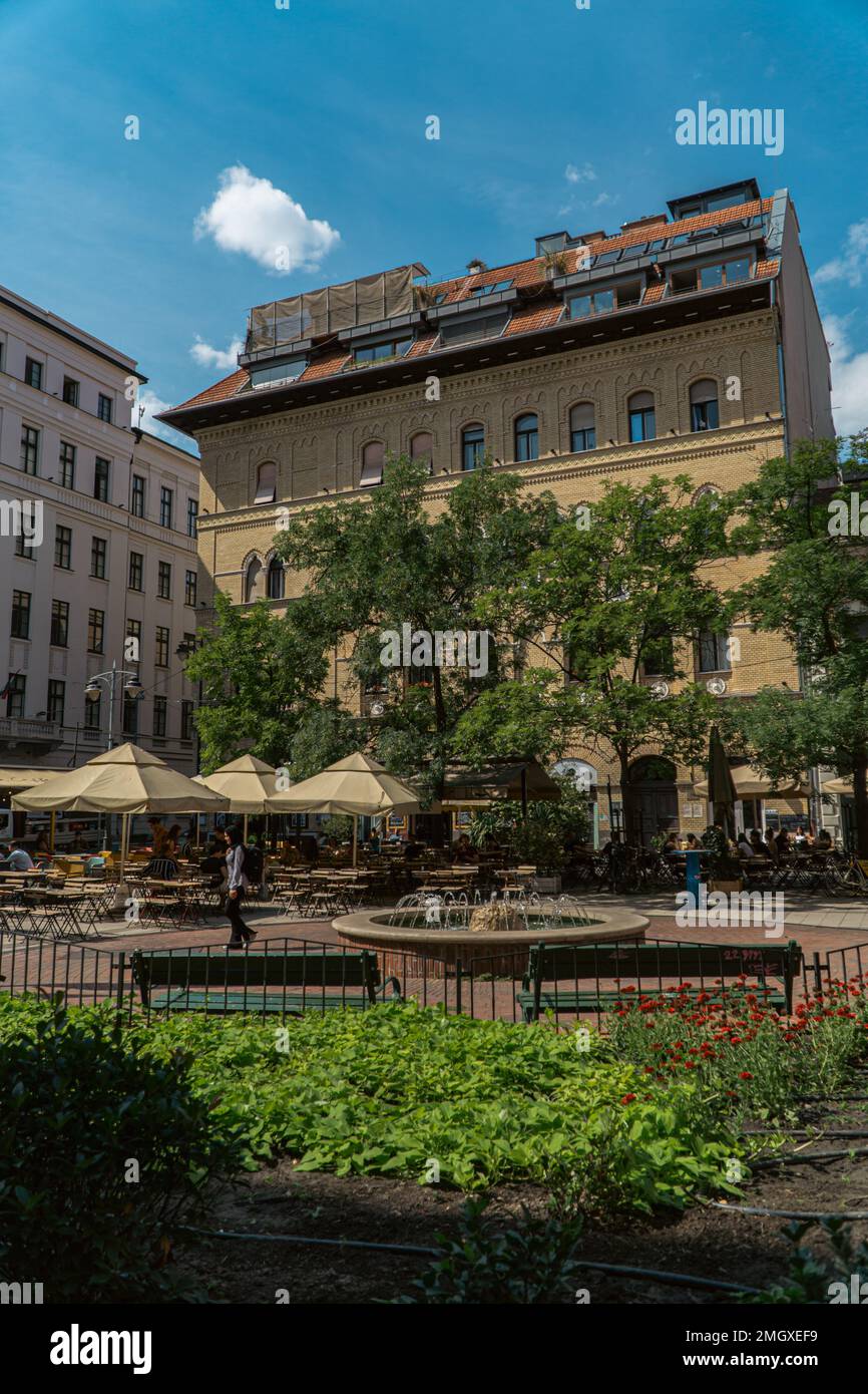 cute little square in the middle of budapest with trees and residential buildings with benches under a blue sky Stock Photo