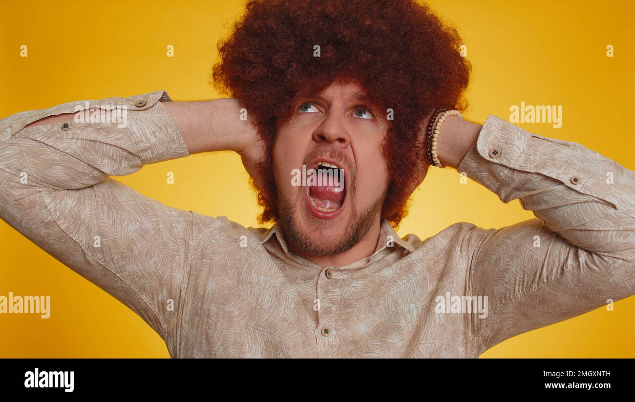 Dont want to hear and listen. Frustrated annoyed irritated man afro hairstyle covering ears and gesturing no, avoiding advice ignoring unpleasant noise loud voices. Hipster guy on yellow background Stock Photo