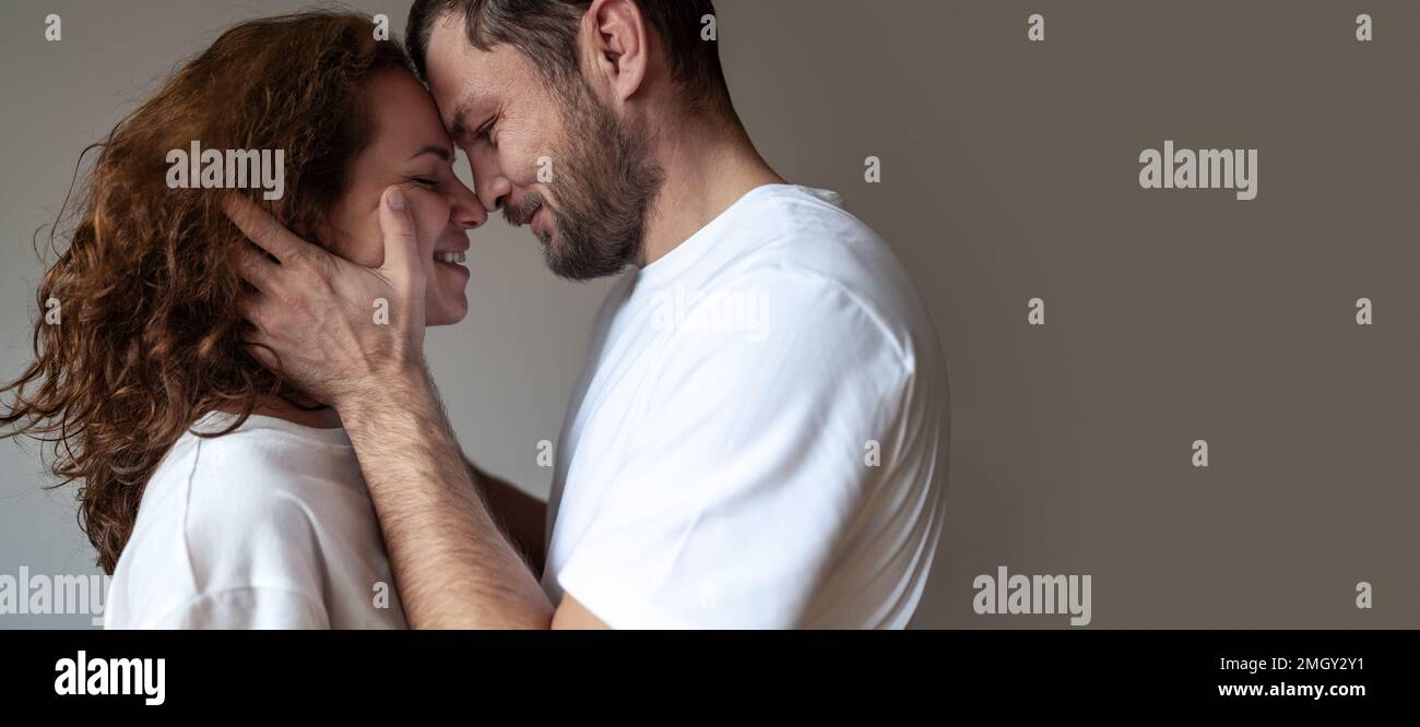 Heterosexual couple in love standing face to face hugging and smiling man gently holding woman's face in his hands. Stock Photo