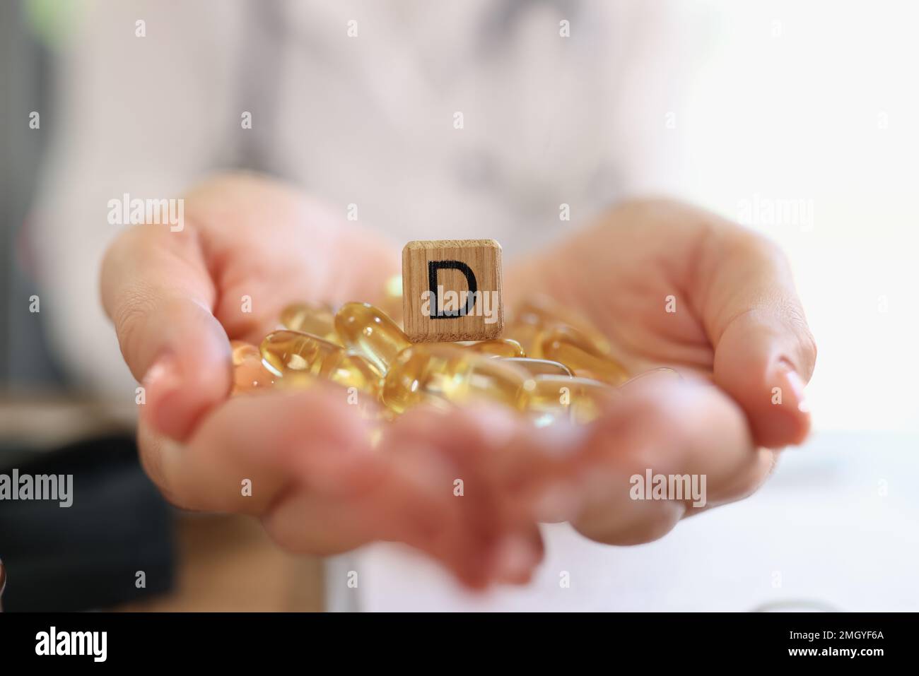 Human hands holding pile of vitamin D capsules with wooden cube with D symbol close up. Stock Photo
