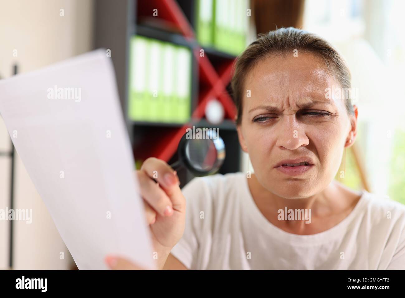 Incredulous middle age woman looking on document trough magnifying glass close-up. Stock Photo