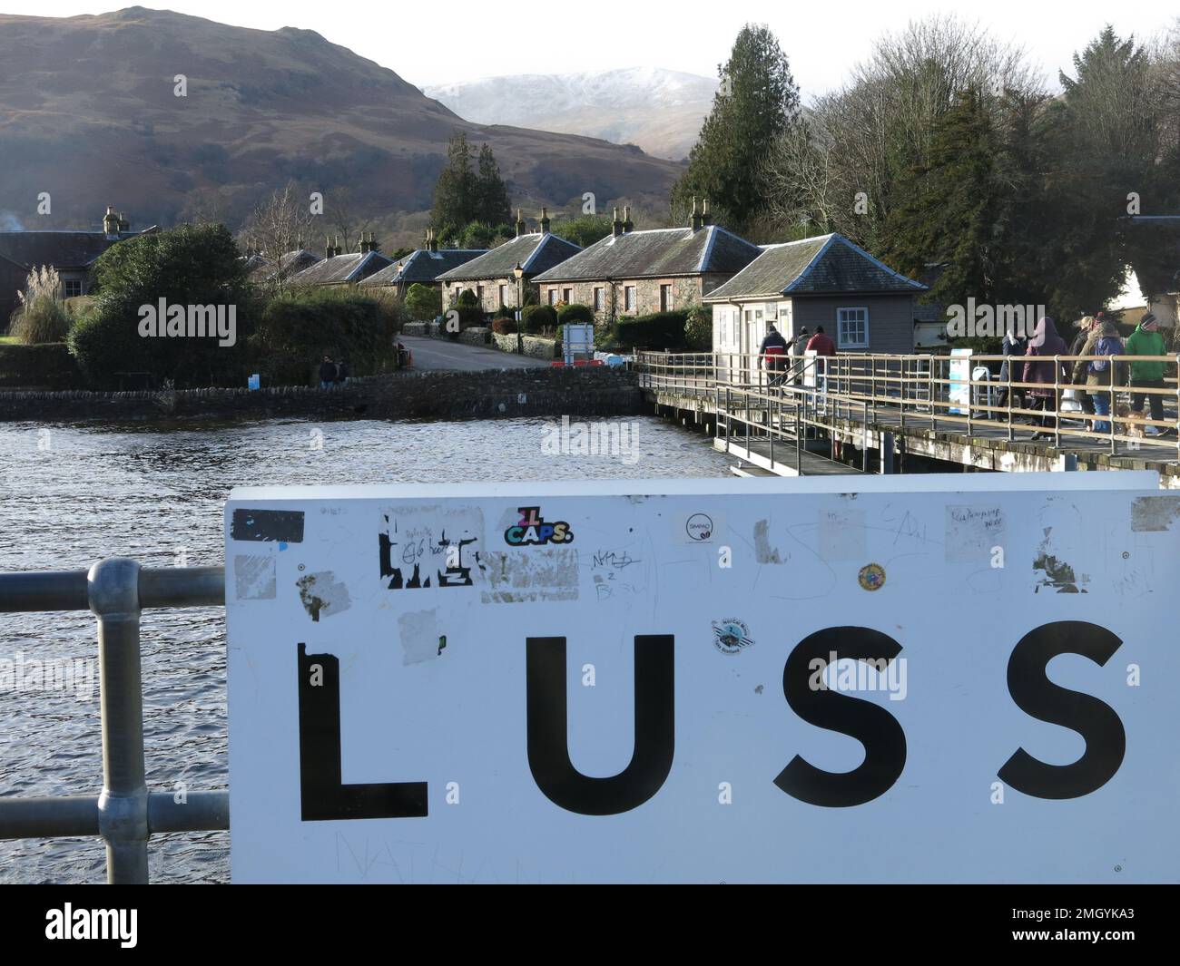 The destination board announcing arrival at the pier of LUSS, with the row of cottages in this quaint conservation village at Loch Lomond. Stock Photo