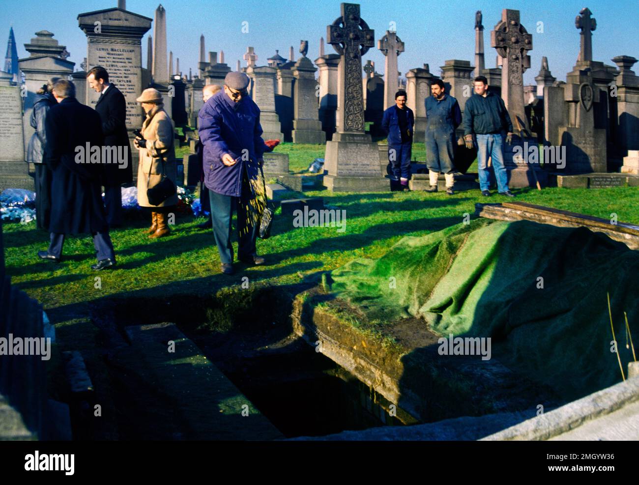 Man Throwing Handful of Earth On to Coffin after Funeral at Cemetery in
