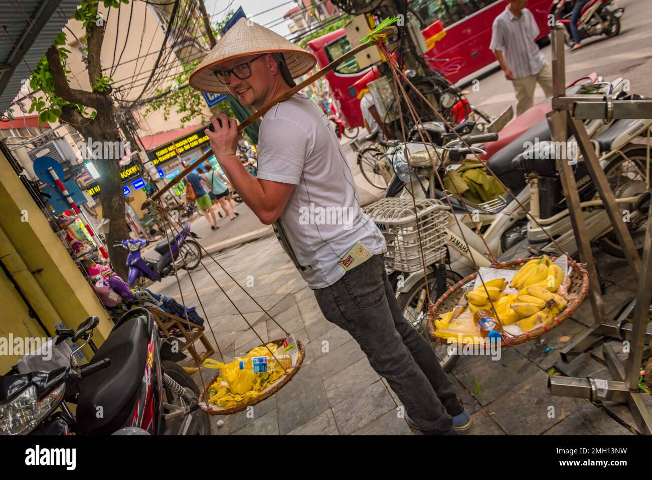Tourist man seen from the side holding traditional Vietnamese shoulder baskets in Hanoi Vietnam Stock Photo