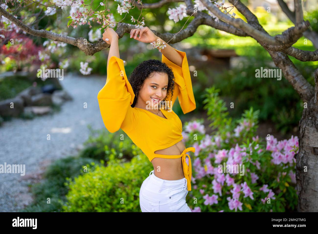 Side View 3/4 Portrait of Young African American Woman with Arms Up in Japanese Style Garden in Spring Stock Photo