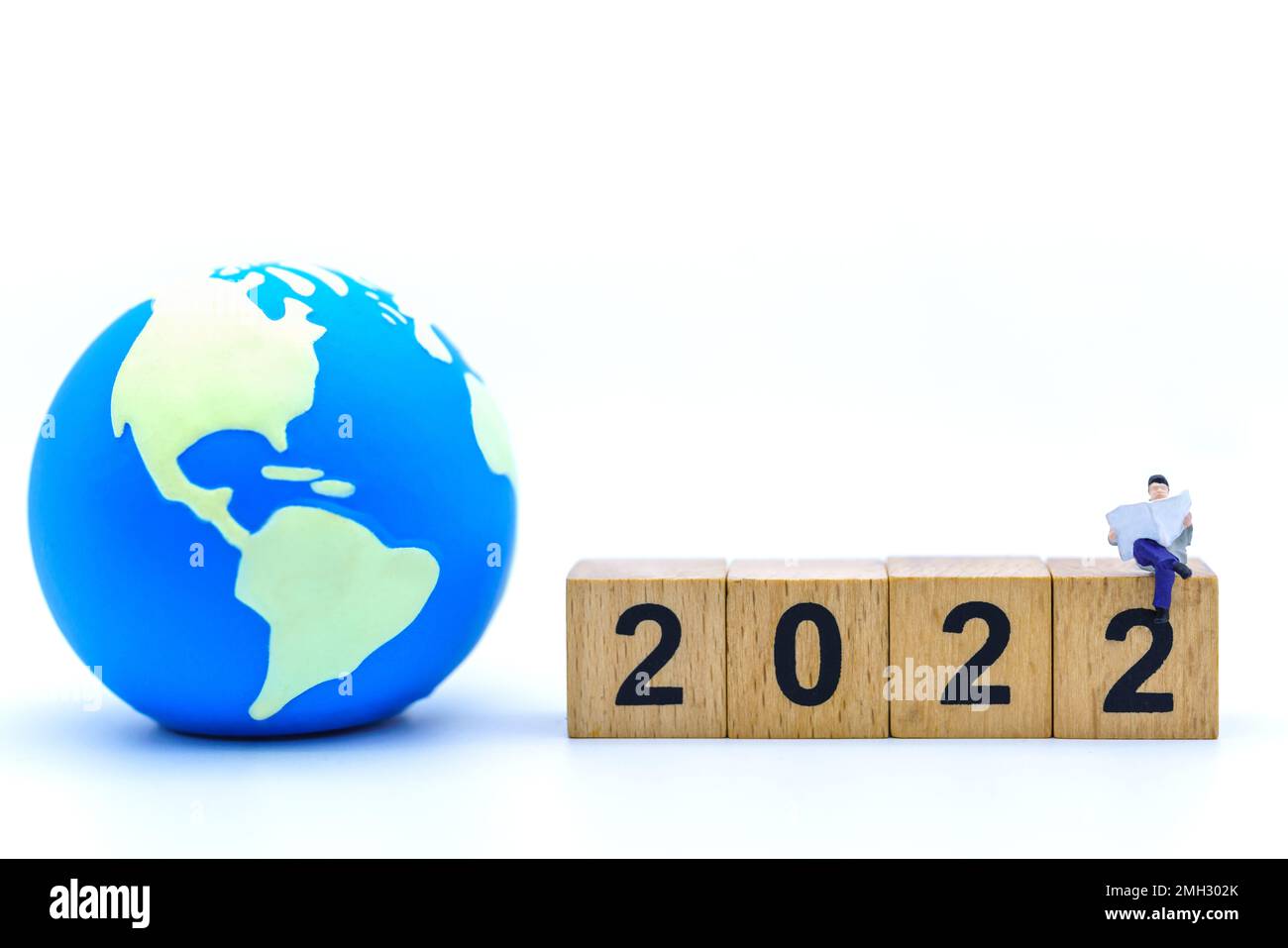 2022 New Year and Business Concept. Closeup of businessman miniature figures sitting and reading a book or newspaper on wooden number block with mini Stock Photo