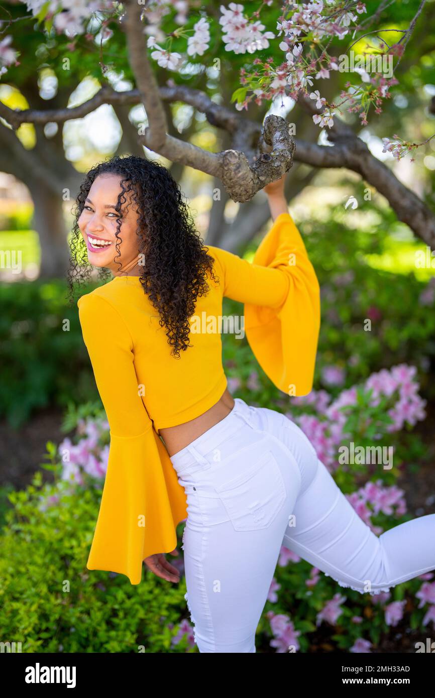 Back View 3/4 Body Portrait of Beautiful Young African American Woman Kicking Leg Back and Holding Blossom Cherry Tree Branch - Spring Stock Photo