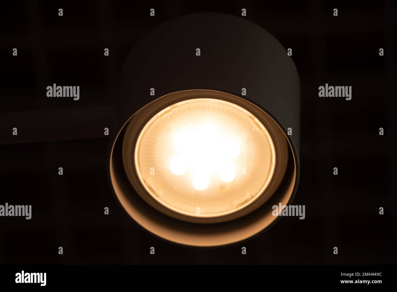 a round white lamp on the ceiling on in the evening, a lamp on in the dark as a background, lamp light at night Stock Photo