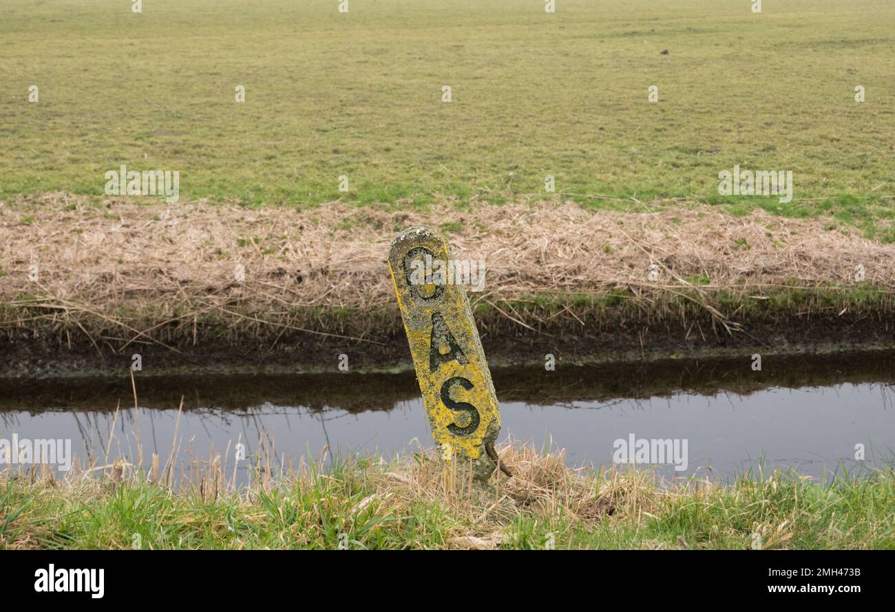 Old, crumbled and crooked bollard for marking an underground gas pipe, on the side of the ditch Stock Photo