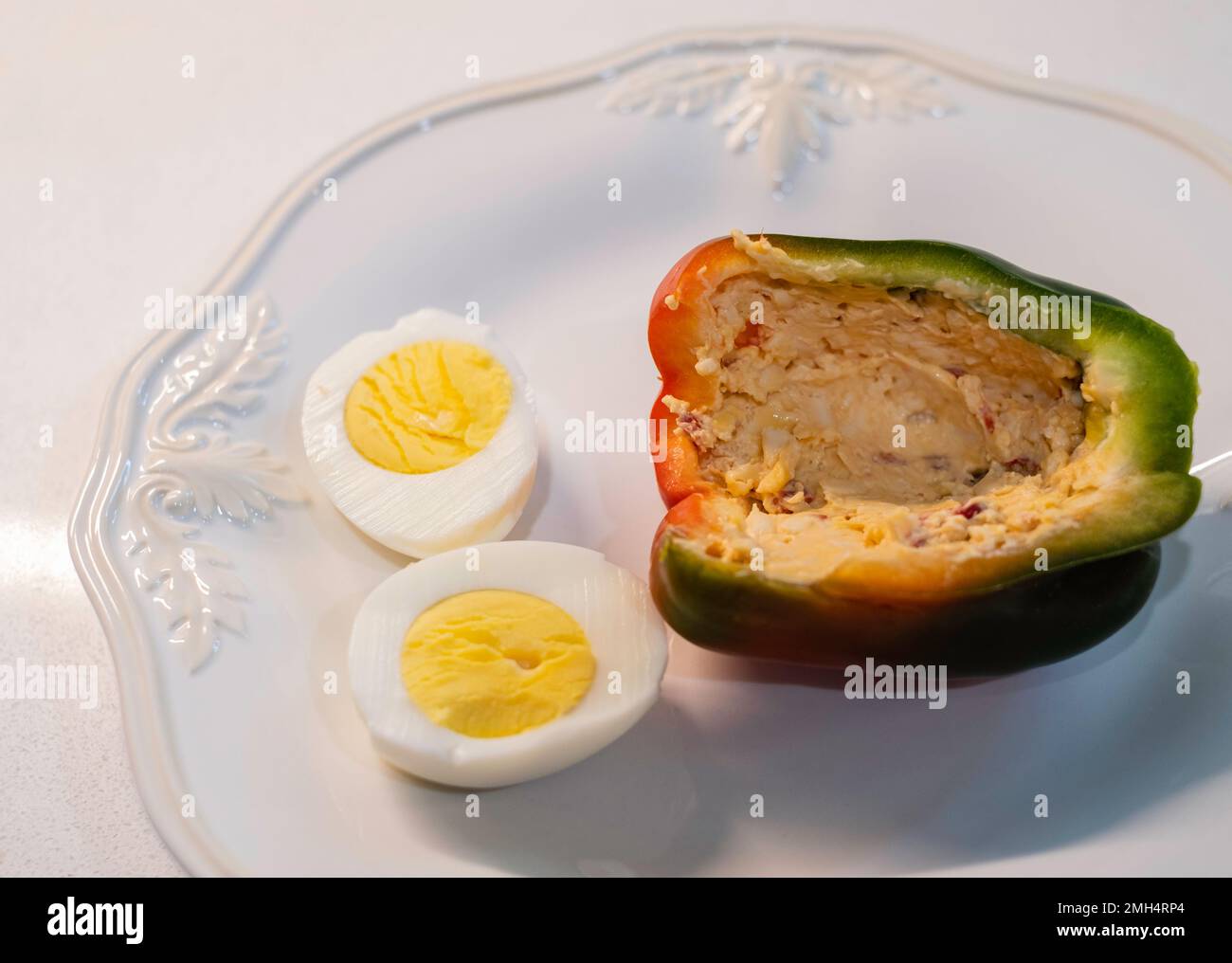 A half of a sweet pepper, a bell pepper, Capsicum annumm, filled with pimento cheese & served on a white dish with a boiled cut egg. Stock Photo