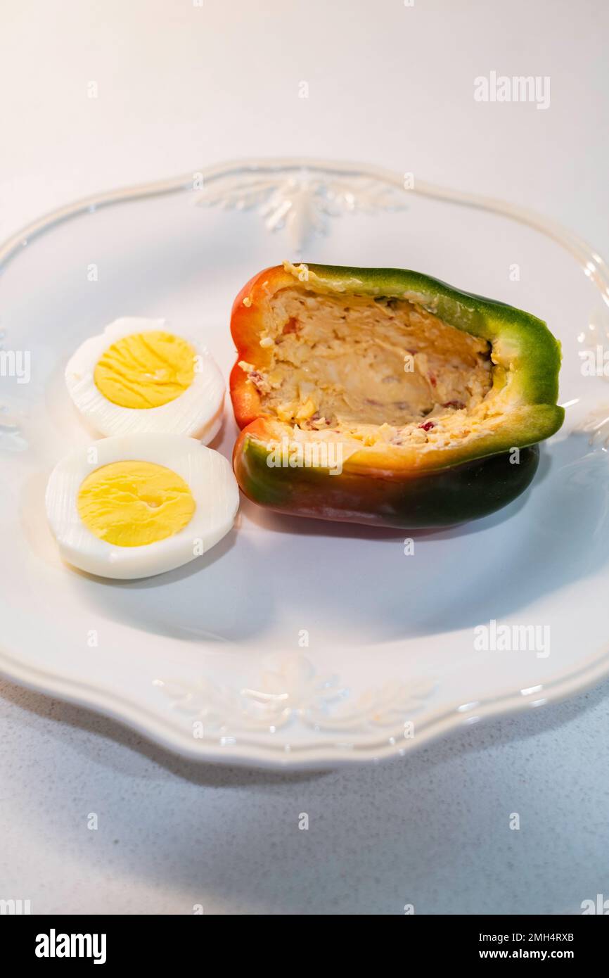 A half of a sweet pepper, a bell pepper, Capsicum annumm, filled with pimento cheese & served on a white dish with a boiled cut egg. Stock Photo