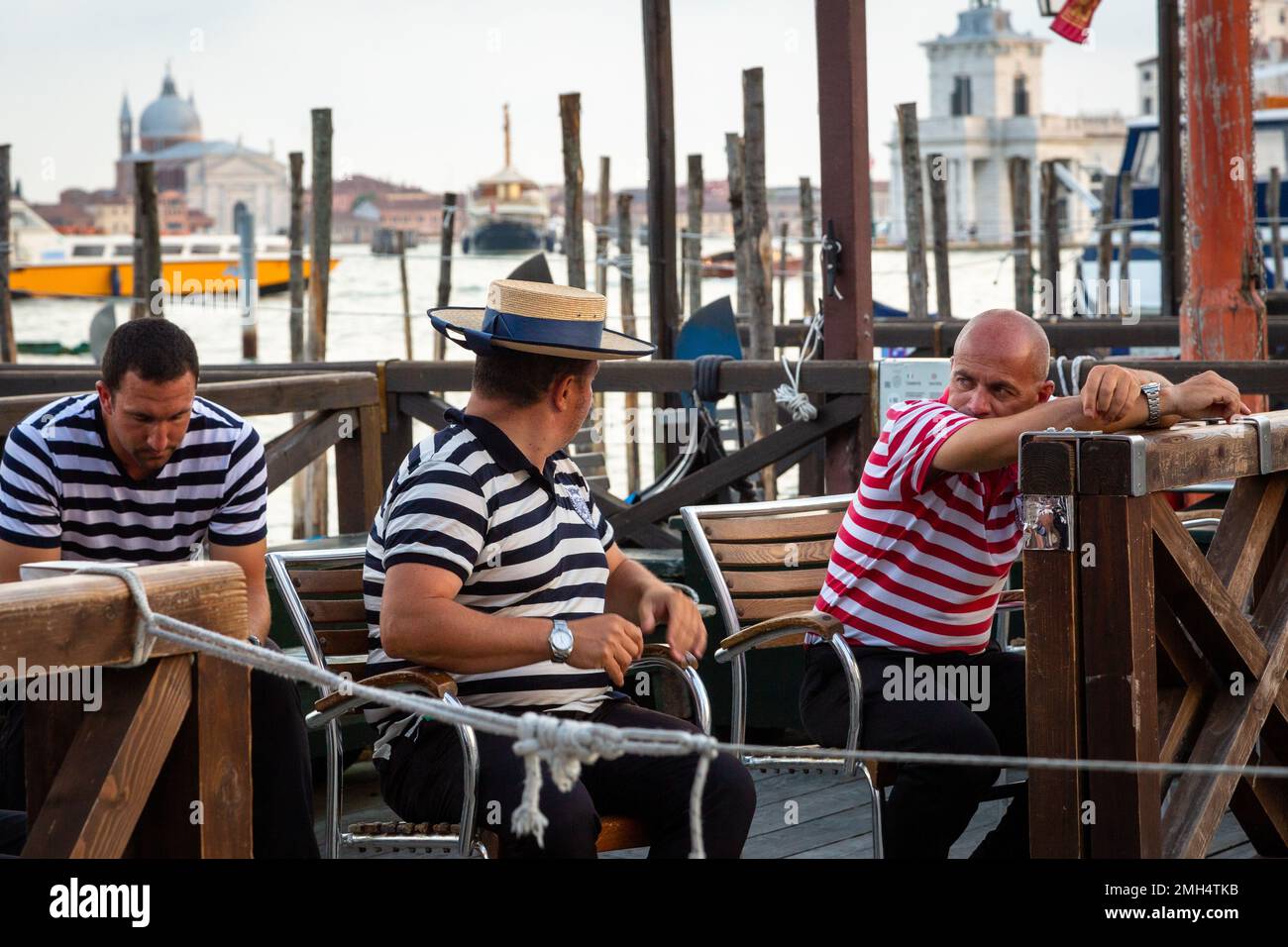 3 Gondoliers waiting for the next customers seated near the lagoon in Venice Stock Photo