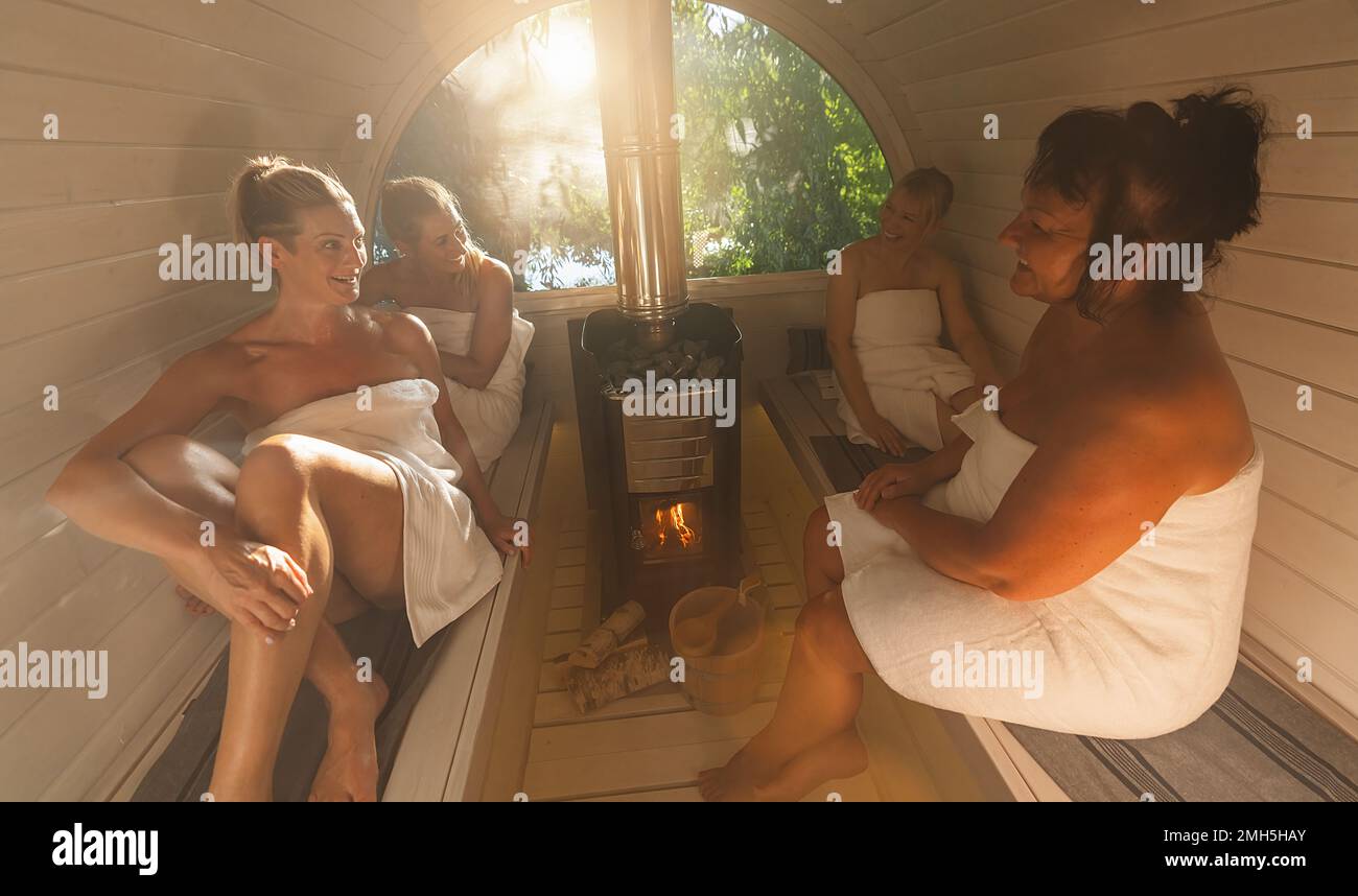 Happy girlfriends relaxing at the wooden barrel sauna in norway. People are relaxed and enjoy the holiday while relaxing in the finnish sauna cabin. Stock Photo